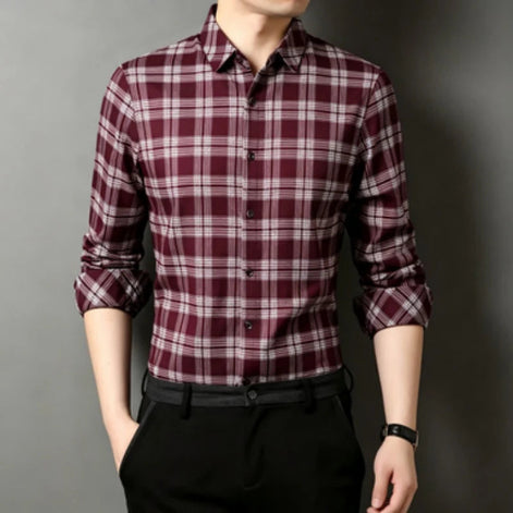 A man wearing a long-sleeve button-up plaid shirt in burgundy and white, paired with black trousers, shown against a dark gray background.