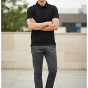 A black short-sleeve polo shirt hanging on a black hanger in a retail clothing display, with other garments visible in the background.