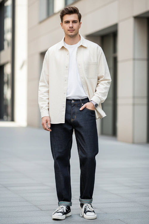 Person wearing blue jeans and white sneakers standing against a wooden wall.