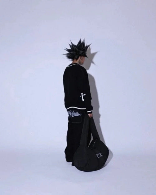 Side-rear view of a model wearing black wide-leg jeans with a white graphic across the upper back, holding a black guitar case against a pale background.