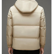 A person shown from the back wearing a light beige hooded puffer jacket against a plain gray studio background.