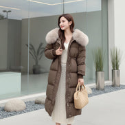 A woman wearing a long brown puffer coat with a large beige fur-trimmed hood, paired with a cream knit dress 
