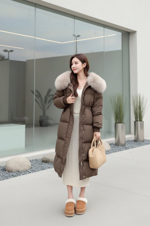 A woman wearing a long brown puffer coat with a large beige fur-trimmed hood, paired with a cream knit dress 