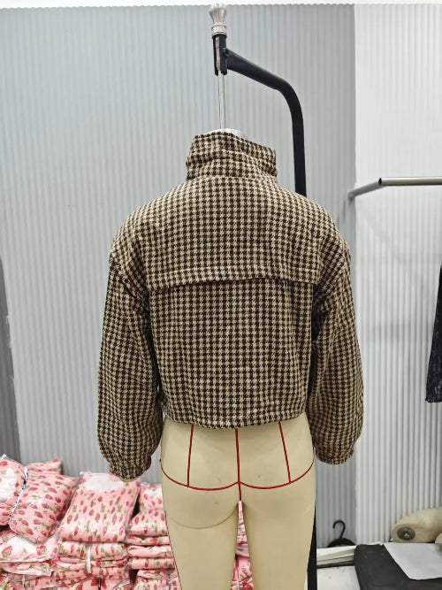 Rear view of a brown and cream houndstooth utility jacket on a dress form, showing a raised collar, back yoke, long sleeves and elasticated cuffs
