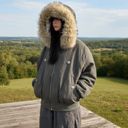 Person wearing a gray parka with a fur-lined hood against a white wall.