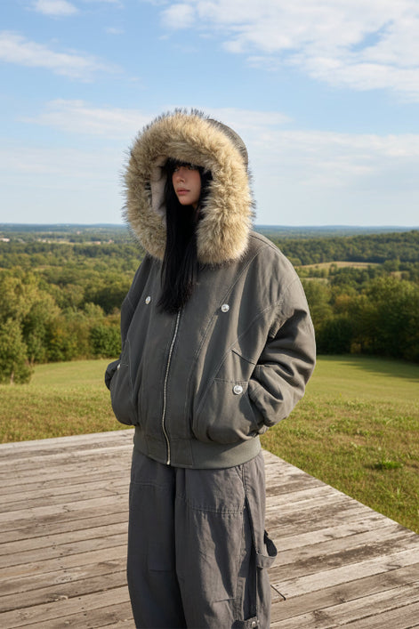 Person wearing a gray parka with a fur-lined hood against a white wall.