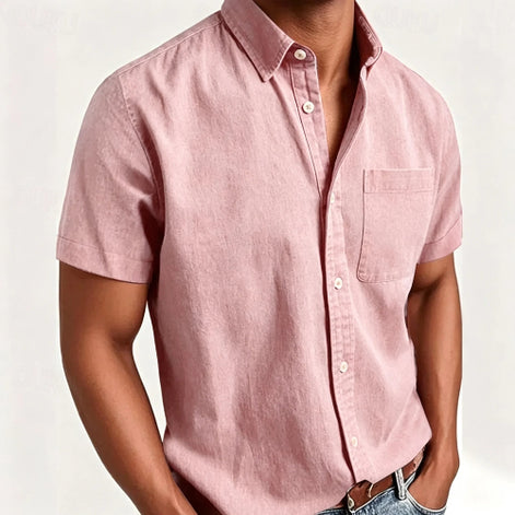 A man wearing a light pink short-sleeve button-up shirt with a chest pocket, paired with blue jeans and a brown leather belt, 