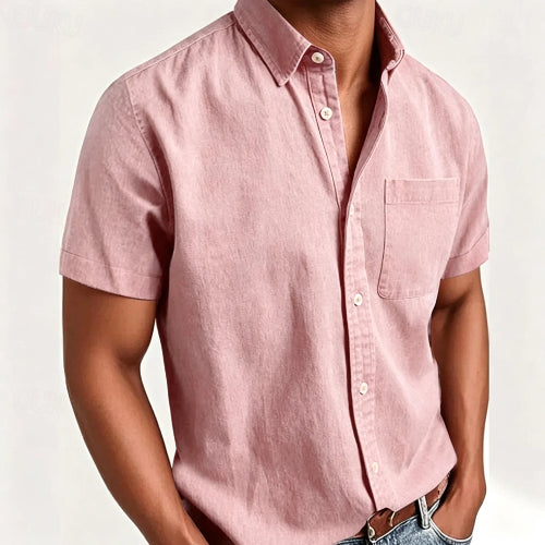 A man wearing a light pink short-sleeve button-up shirt with a chest pocket, paired with blue jeans and a brown leather belt, 