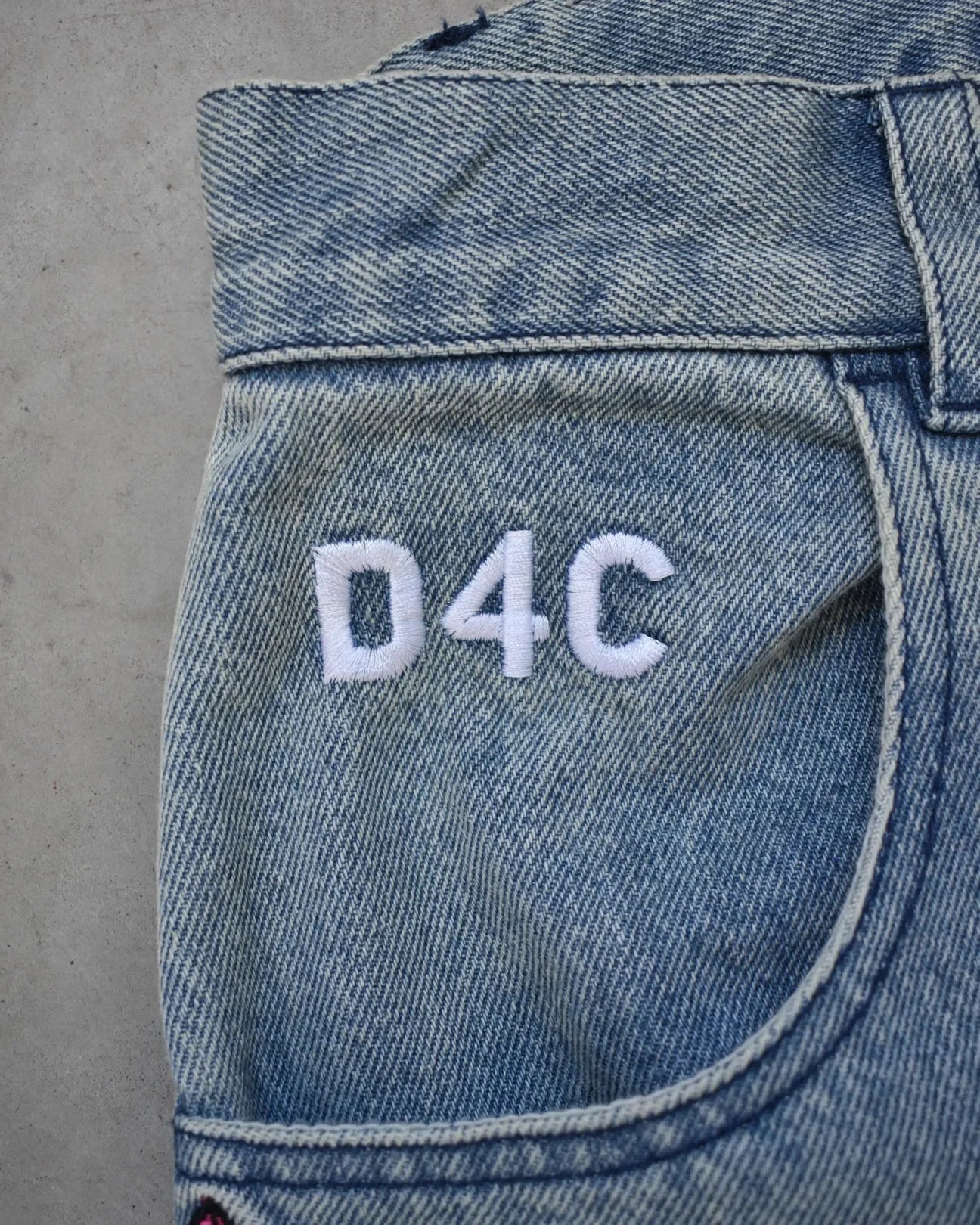 Close-up of blue denim fabric with 'D4C' embroidery on a gray background