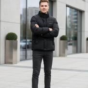 A black puffer jacket hanging on a clothing rack in a retail store setting, with promotional graphic overlays on the left highlighting warmth, softness, and down content. The jacket has a high collar, front zipper and snap closure, and a small chest label.