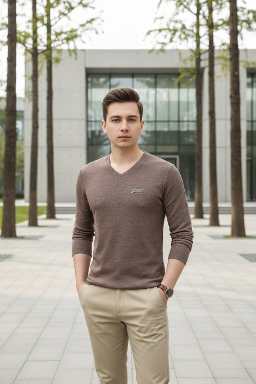 Man wearing a brown V-neck sweater with a logo on a gray background