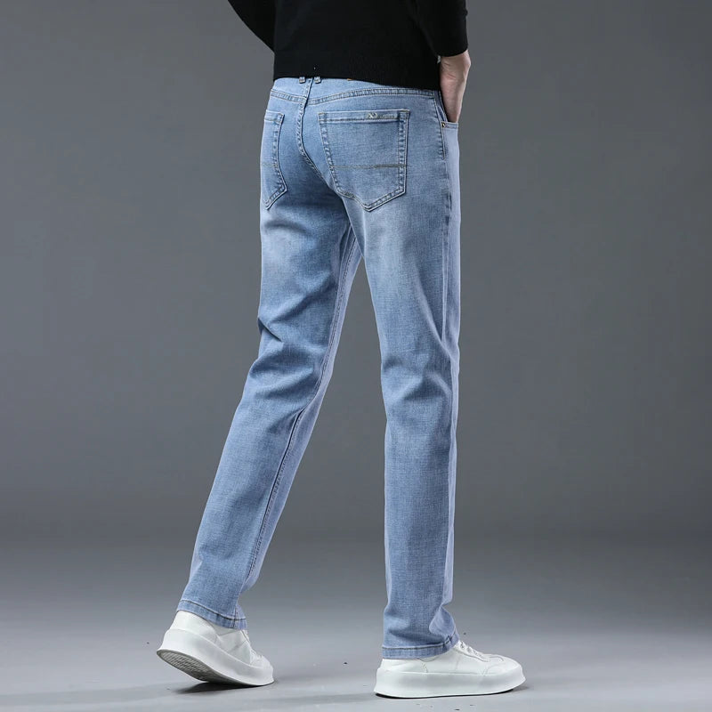 A person wearing light blue slim-fit jeans, a black long-sleeve top, and white sneakers, shown from the back against a gray studio background.