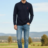 Navy long-sleeve polo shirt with red logo on a hanger against a rack of other shirts.