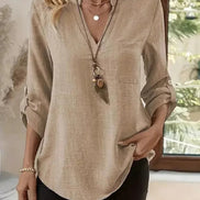 Woman wearing a beige blouse with a pendant necklace in a blurred indoor setting