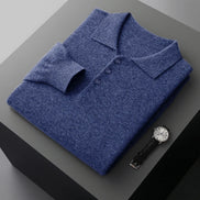 A folded blue knit polo shirt displayed on a dark gray pedestal, with a wristwatch placed beside it on a light gray background.