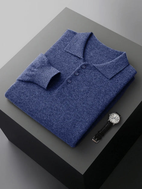 A folded blue knit polo shirt displayed on a dark gray pedestal, with a wristwatch placed beside it on a light gray background.