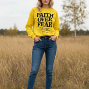 Yellow sweatshirt with 'Faith Over Fear' text on a wooden background