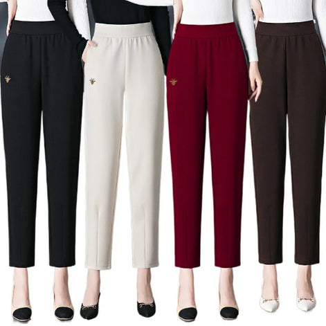 Four women modeling straight-leg cropped pants in black, off-white, burgundy, and dark brown, each with a small gold bee emblem on the upper left leg.