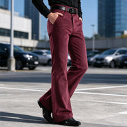A person wearing burgundy corduroy pants with a black belt and black dress shoes, standing in an outdoor parking lot.