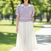 A woman wearing a light purple short-sleeve ribbed knit polo sweater over a white collared shirt, paired with a black polka-dot skirt and carrying a black shoulder bag.