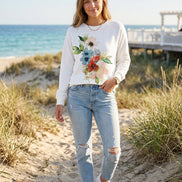 A woman wearing a white long-sleeve sweatshirt with a large watercolor floral print in shades of blue, red, pink, and green, 