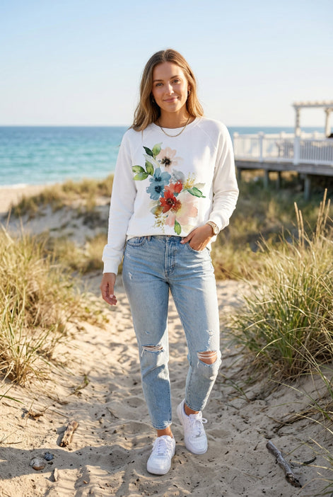 A woman wearing a white long-sleeve sweatshirt with a large watercolor floral print in shades of blue, red, pink, and green, 