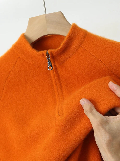 Orange fleece pullover with a zipper on a hanger, held by a hand.