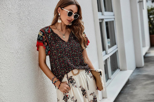 Woman wearing a floral top and denim shorts, standing against a textured wall.