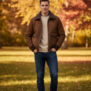 A brown suede and shearling jacket laid flat on grass, with a red and black 'BEKE DEKE' logo overlay in the top-left corner.