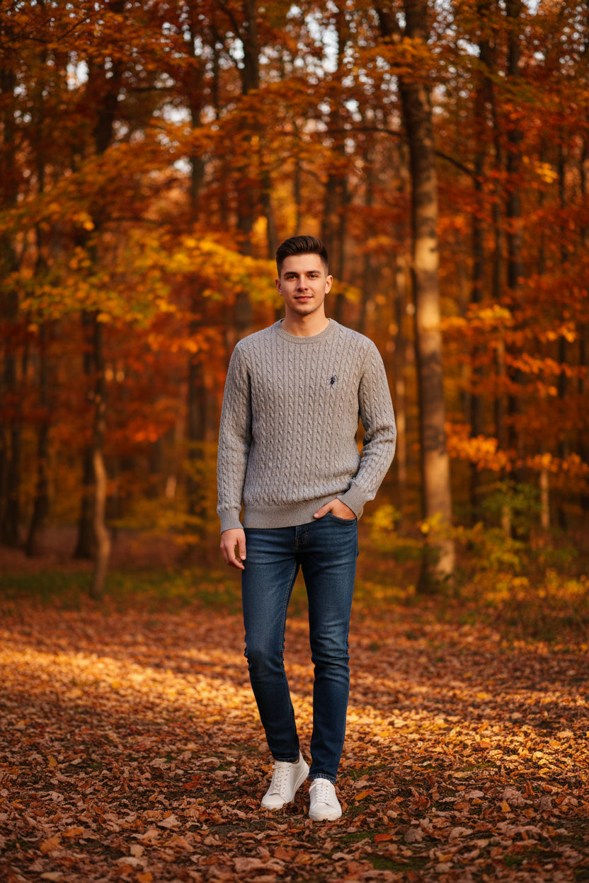 Gray cable knit sweater with a brand logo on a hanger against a wooden background.