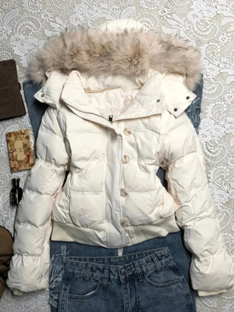 An off-white puffer jacket with a fluffy beige faux-fur trimmed hood, styled flat-lay on top of blue jeans against a white lace-patterned background.