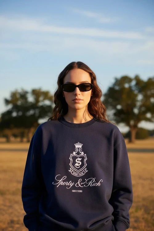 Person wearing navy blue sweatshirt and shorts with a logo, standing against a white background