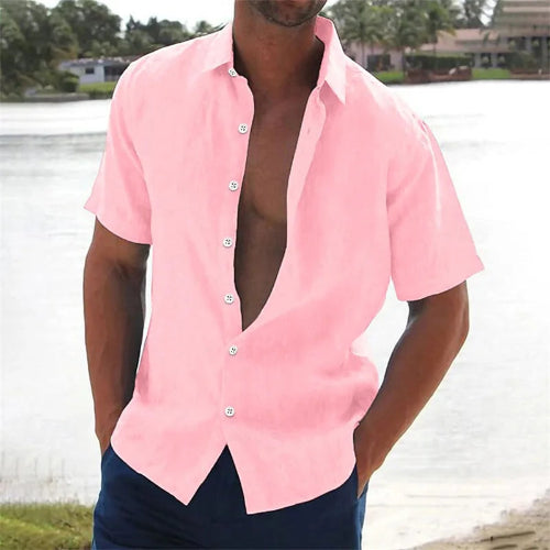 Man wearing a pink button-up shirt with open collar by a body of water.