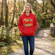 A bright red pullover hoodie laid flat on a dark textured surface, featuring a colorful 'Family Christmas 2026' graphic with a Santa hat and floral accents. 