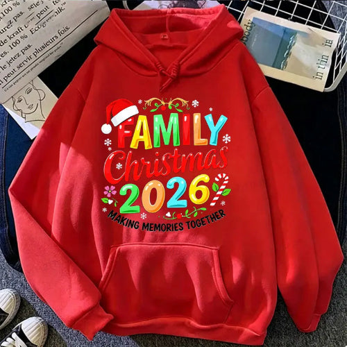 A bright red pullover hoodie laid flat on a dark textured surface, featuring a colorful 'Family Christmas 2026' graphic with a Santa hat and floral accents. The hoodie includes a drawstring hood and a front 