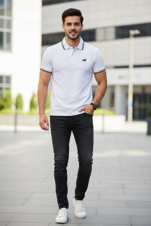 Man wearing a white polo shirt with black trim and 'King' logo, standing against a blurred background.