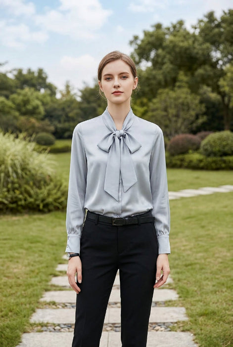 Woman wearing a light gray blouse with a bow tie, sitting indoors.