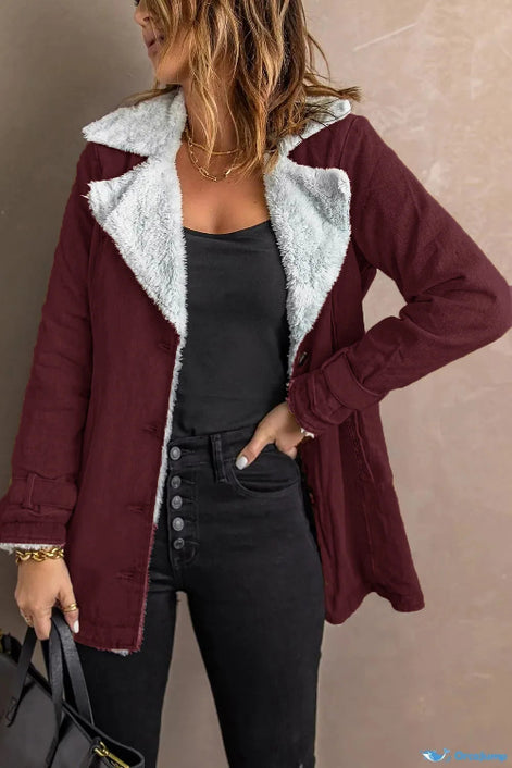 Woman wearing a dark red jacket with white fleece-look lining, wide lapels and buckled cuffs over a black top and jeans