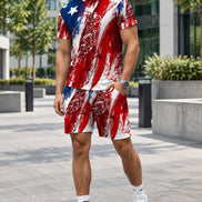 A man modeling a matching red, white, and blue distressed American flag t-shirt and shorts set, paired with white socks and sneakers, standing against a gray paneled wall.