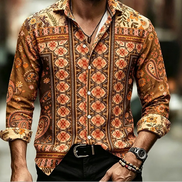 A man wearing a long-sleeve button-up shirt with an intricate orange, brown, and beige geometric and paisley pattern, paired with black pants and accessories.