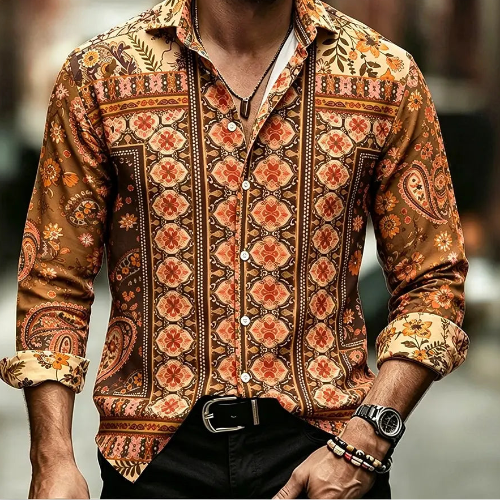 A man wearing a long-sleeve button-up shirt with an intricate orange, brown, and beige geometric and paisley pattern, paired with black pants and accessories.