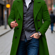 A man wearing a vibrant green double-breasted overcoat over a gray button-down shirt, white t-shirt, and blue jeans, walking on a blurred city street.