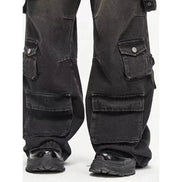 Close-up of washed black baggy cargo jeans showing buttoned side pockets, large lower-leg flap pockets, and wide hems over chunky black shoes.⠋
