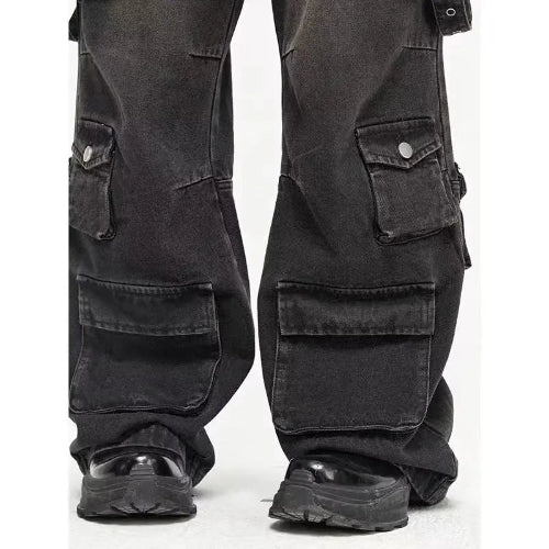 Close-up of washed black baggy cargo jeans showing buttoned side pockets, large lower-leg flap pockets, and wide hems over chunky black shoes.⠋