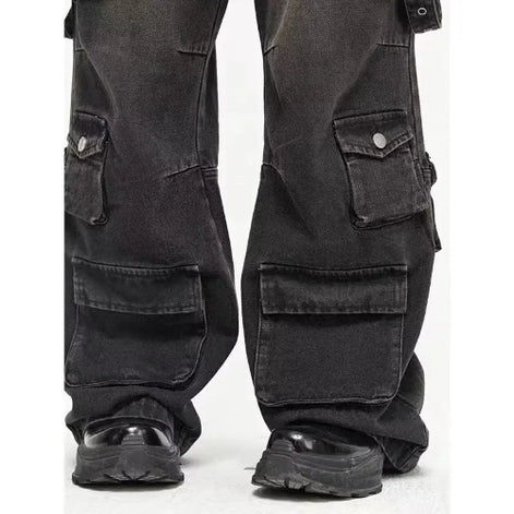 Close-up of washed black baggy cargo jeans showing buttoned side pockets, large lower-leg flap pockets, and wide hems over chunky black shoes.⠋