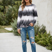 A woman wearing a long-sleeve crewneck sweatshirt with a black and white tie-dye pattern, paired with blue jeans and holding a bouquet of white roses.