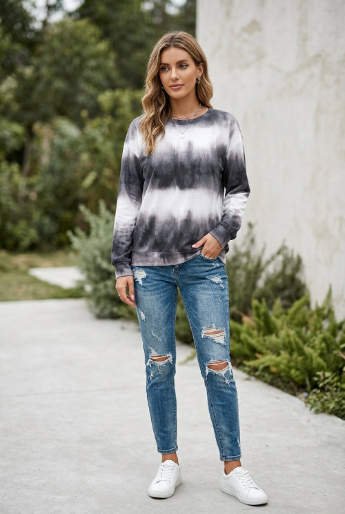 A woman wearing a long-sleeve crewneck sweatshirt with a black and white tie-dye pattern, paired with blue jeans and holding a bouquet of white roses.
