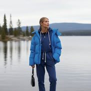 Person wearing a blue puffer jacket and tracksuit standing against a building.