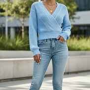 A woman wearing a light blue knit wrap sweater with cable details and light-wash blue jeans, 