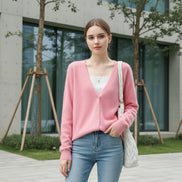 A pink fuzzy V-neck cardigan sweater worn by a model, styled over a white ribbed top and paired with a white woven handbag, 